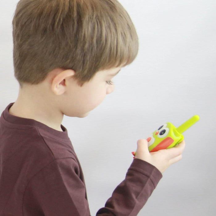 Profile of a child holding a bright green owl-shaped walkie-talkie with orange wings and large eyes.
