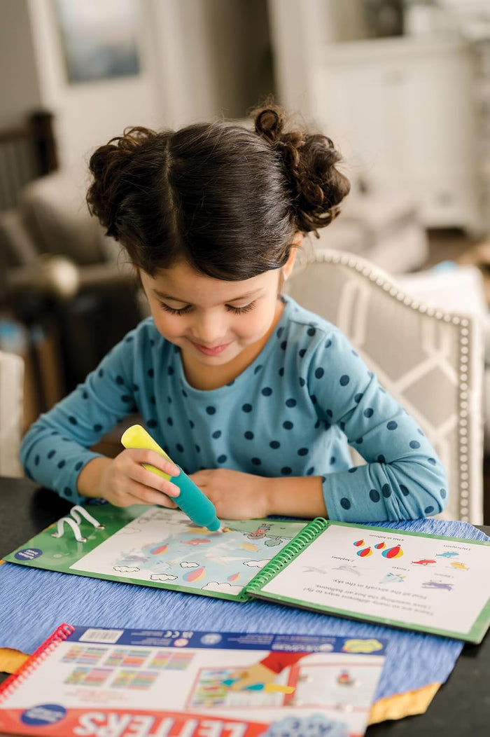 Child uses a chunky blue and yellow water pen to reveal colorful illustrations in a spiral-bound activity book.