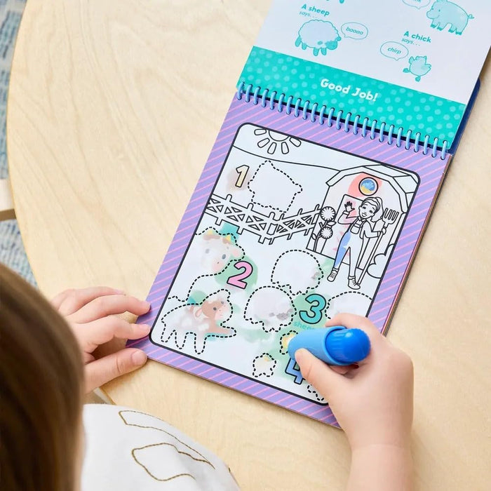 Child's hands coloring a spiral-bound Ms. Rachel activity book with a blue water pen to reveal farm animals.