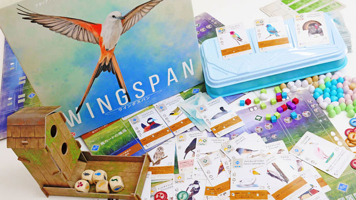 Wingspan board game box with bird art, cards, a birdhouse dice tower, and small colorful egg-shaped pieces.