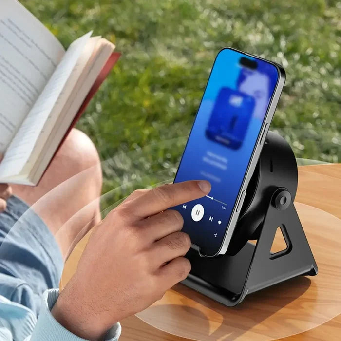 Person using a smartphone with Wireless Induction Speaker with Bluetooth-compatible Speaker while reading a book outdoors.