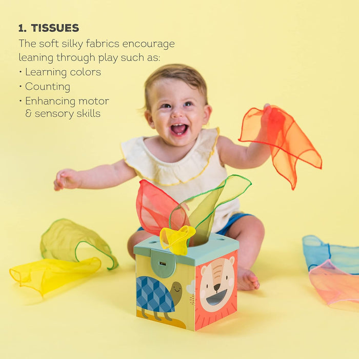 Happy baby playing with a toy tissue box with lion and turtle designs and colorful, translucent fabric scarves.