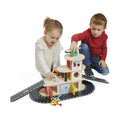 Two children play with a multi-level wooden toy garage featuring colorful accents, grey ramps, and a helipad.