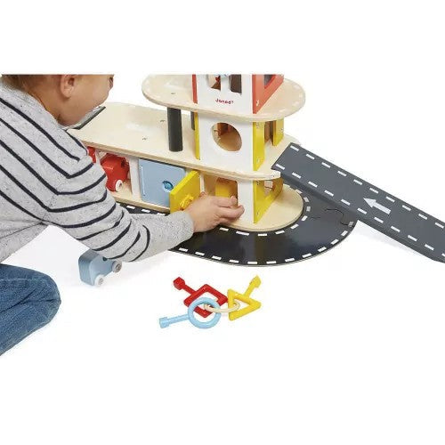 A child plays with a multi-level wooden toy garage featuring colorful doors, a grey ramp, and a set of toy keys.