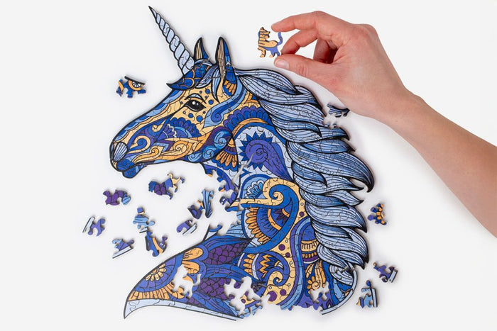 Intricate blue and gold wooden unicorn puzzle with ornate patterns and a hand holding a cat-shaped piece.
