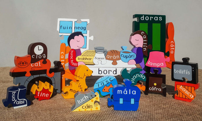 Colorful wooden stand-up puzzle pieces with Irish labels for home objects, people, and pets on a burlap surface.
