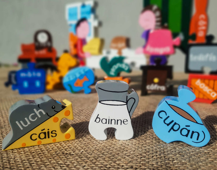 Hand-painted wooden puzzle pieces with Irish words for mouse, cheese, milk, and cup on a textured burlap surface.
