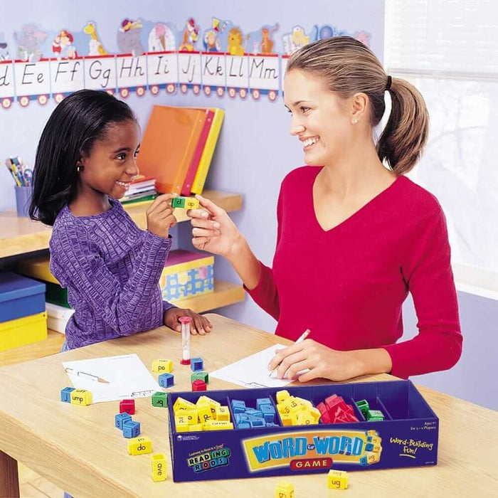 A woman and girl sit at a table using colorful interlocking phonics rods from an open blue game box.