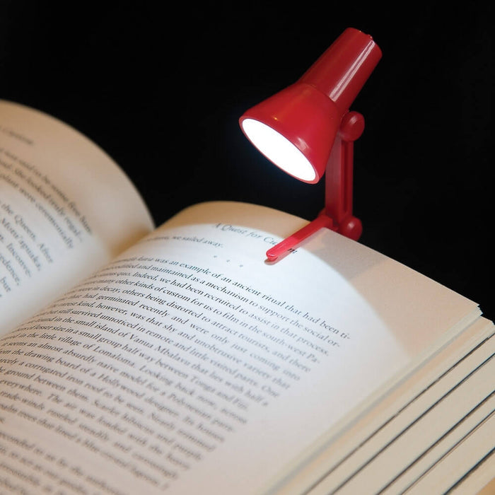 Miniature red clip-on reading light shaped like a desk lamp, shining a bright light on an open book.