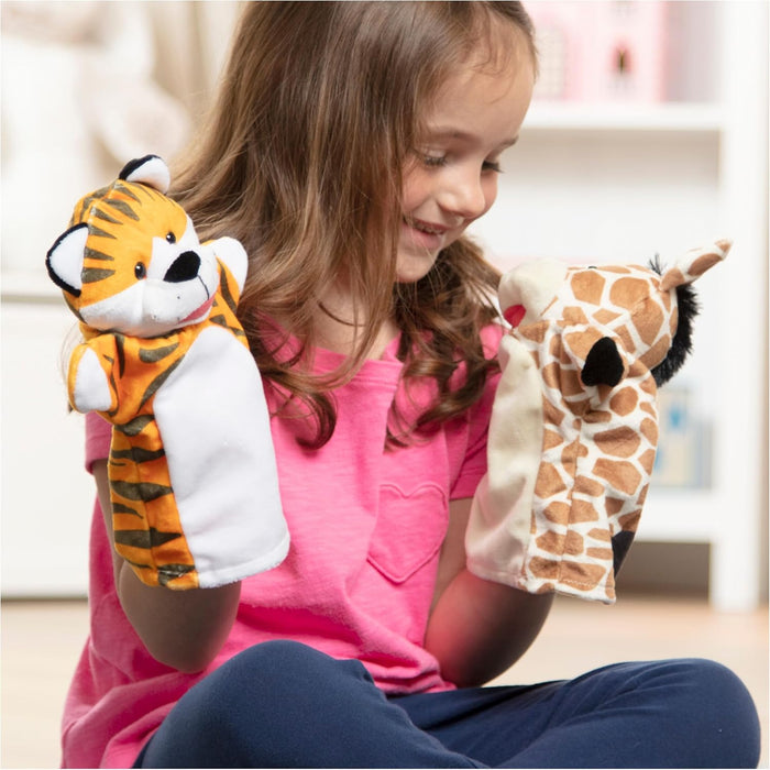 A young girl playing with a plush orange striped tiger puppet and a brown spotted giraffe hand puppet.
